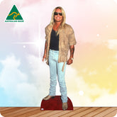 Cardboard cutout of a person wearing sunglasses and casual clothing on a wooden floor with a colorful background.